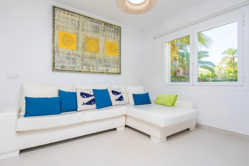 Una sala luminosa con asientos blancos y cojines de colores junto a una ventana grande.