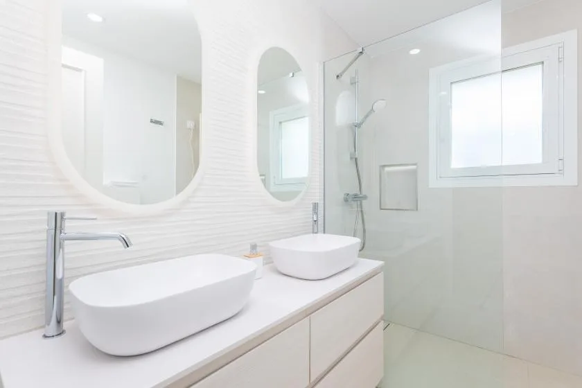 Un baño luminoso con un tocador largo, dos lavabos y una ducha de vidrio.