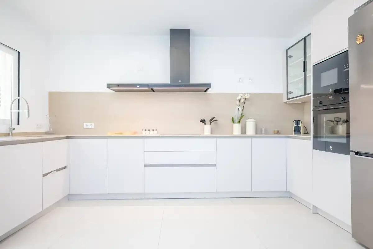 Una cocina moderna y luminosa con armarios blancos y electrodomésticos integrados.
