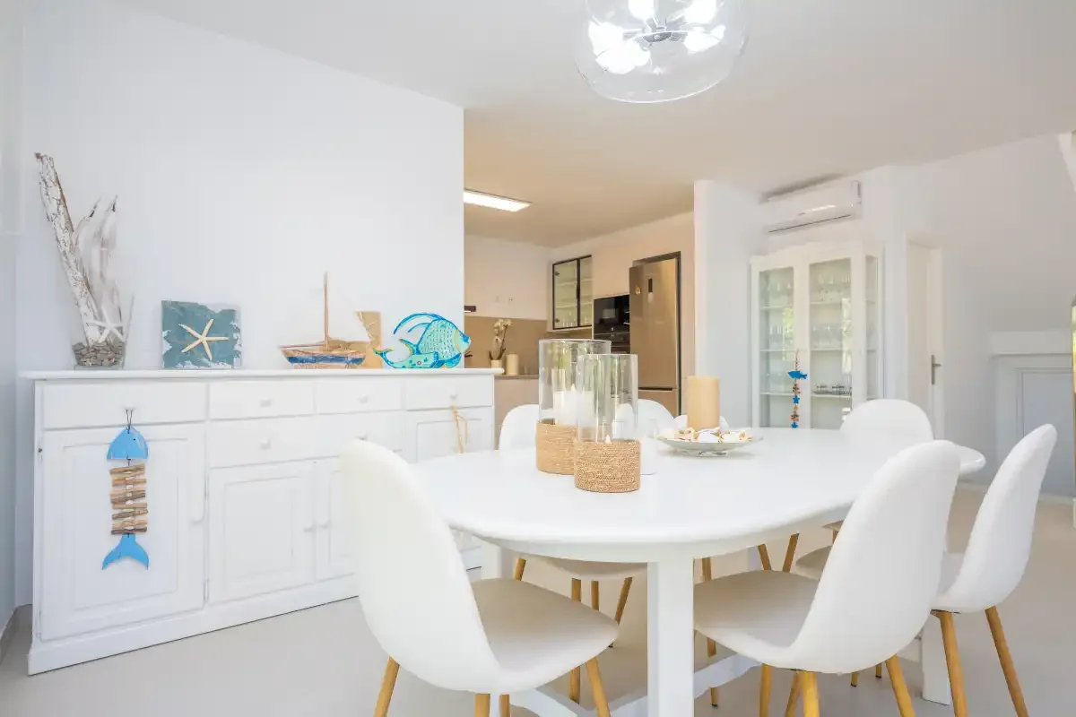 Un comedor luminoso con una mesa blanca y sillas junto a un aparador decorado.