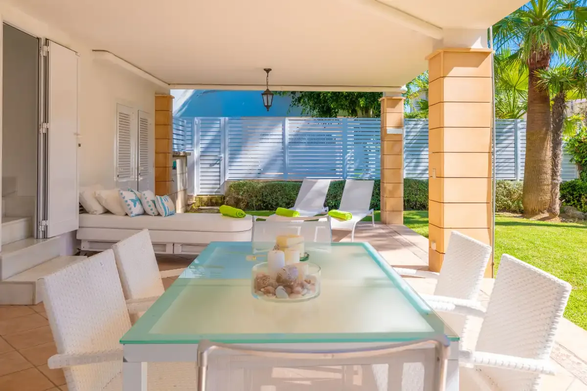 Comedor exterior cubierto con una mesa, asientos y un jardín al fondo.