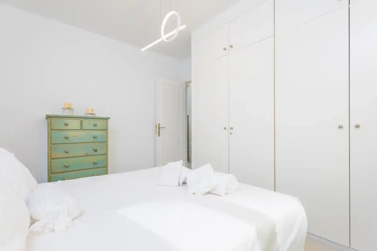 Un dormitorio luminoso con ropa de cama blanca y una cómoda verde.