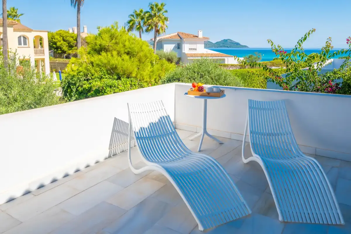 Una terraza soleada con asientos azules mira hacia la vegetación y el mar.