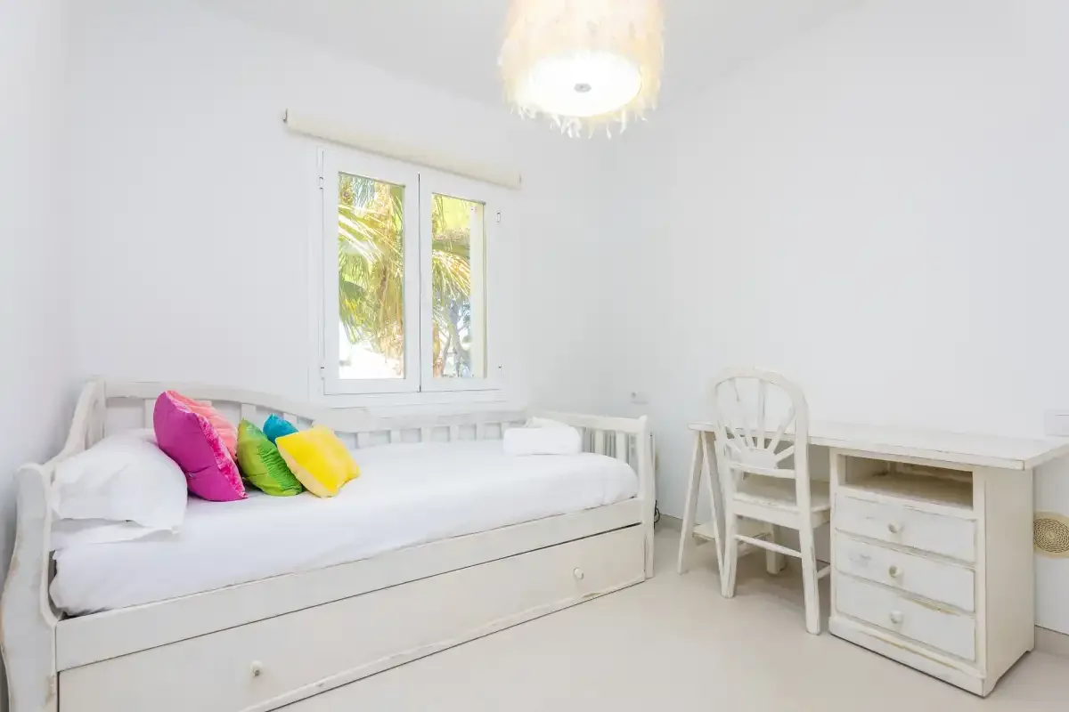 Un dormitorio luminoso con una cama blanca bajo una ventana.