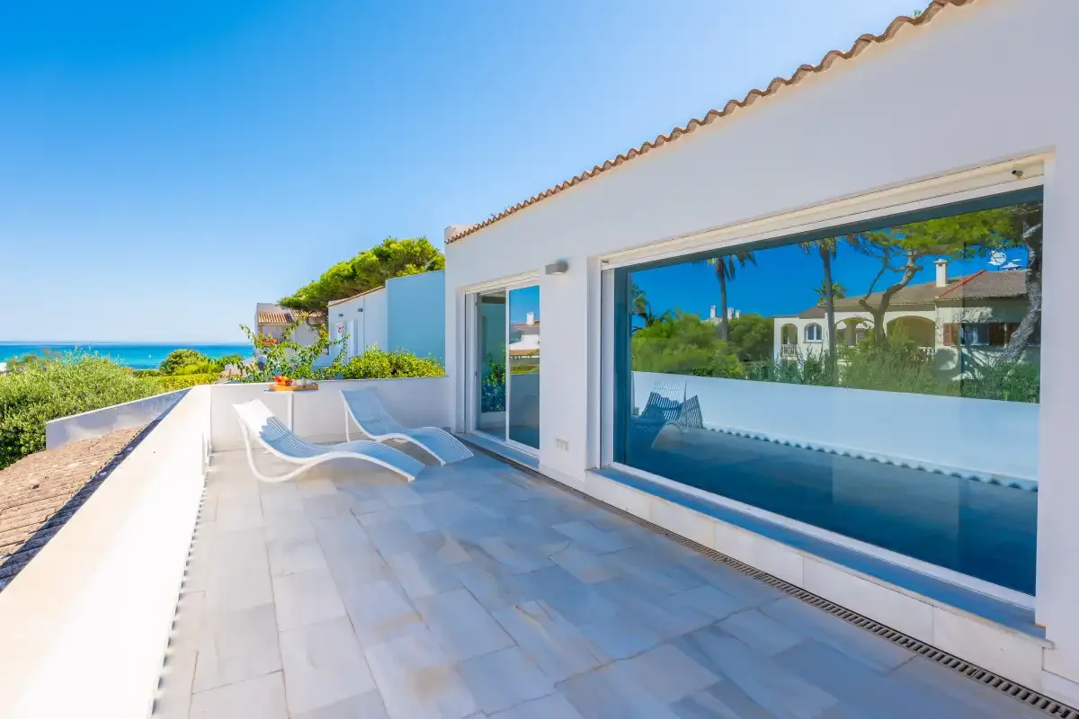 Una terraza soleada junto a un edificio blanco, con tumbonas y vistas al mar.