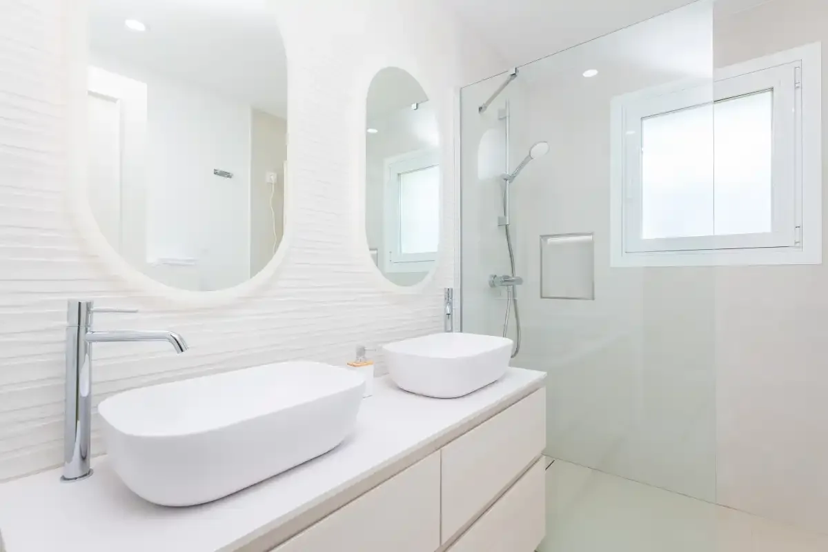 Un baño luminoso con un mueble largo, dos lavabos y una ducha de vidrio.
