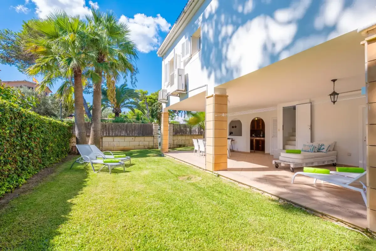 Una casa da a un patio soleado con jardín y asientos al aire libre.