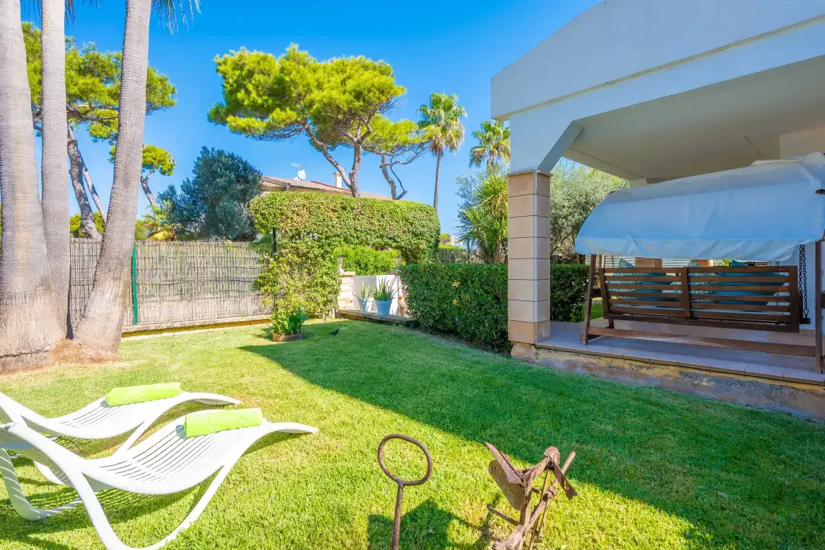Un jardín soleado con asientos sobre el césped junto a un patio cubierto.