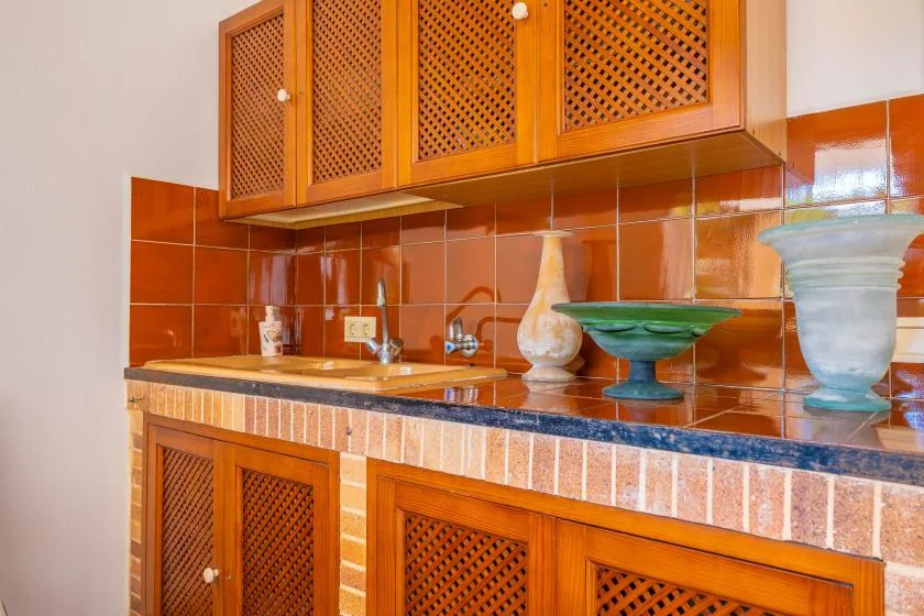 Una encimera de cocina con azulejos está bajo armarios de madera con celosía.