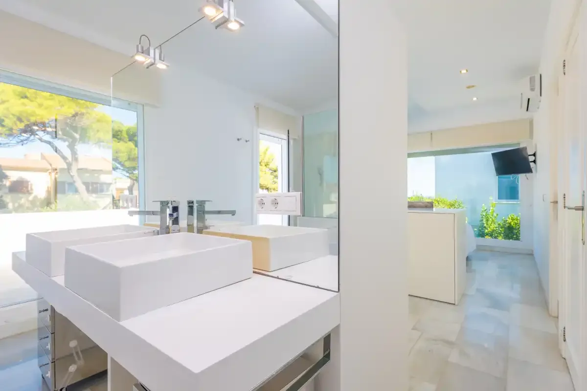 Un baño luminoso con dos lavabos y una gran ventana con vistas a la vegetación.