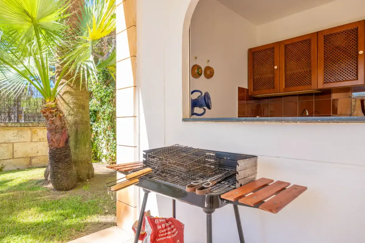 Una parrilla al aire libre está junto a una palmera y una encimera de azulejos.