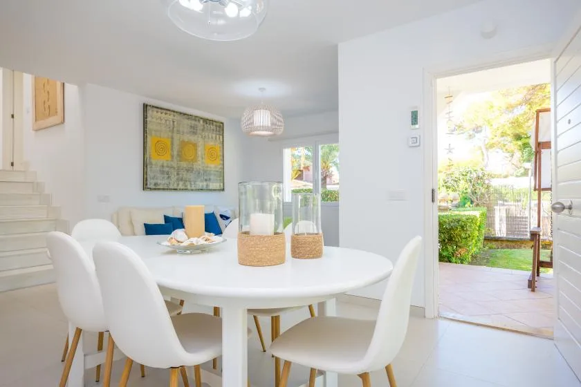 Un comedor luminoso con una mesa blanca y una puerta abierta al jardín.