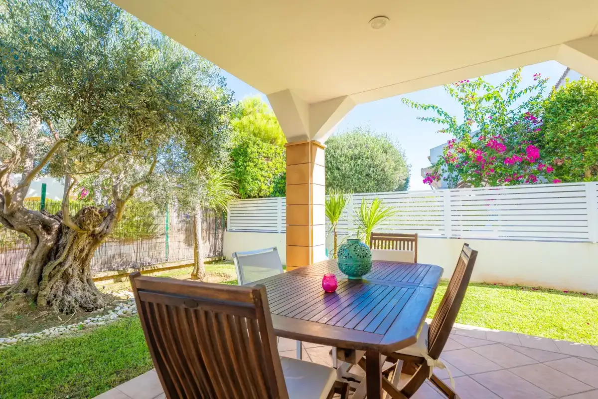 Una zona de comedor exterior a la sombra, con mesa de madera y vistas al jardín.