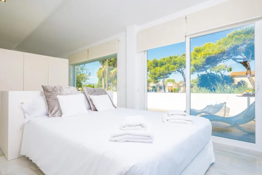 Un dormitorio luminoso con una cama bien hecha junto a grandes ventanas.