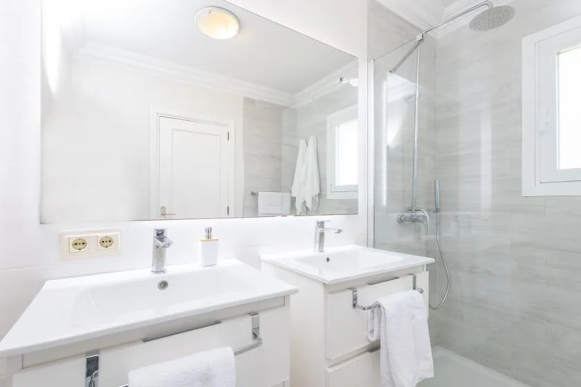Un baño luminoso tiene dos lavabos y una ducha con mampara de vidrio.