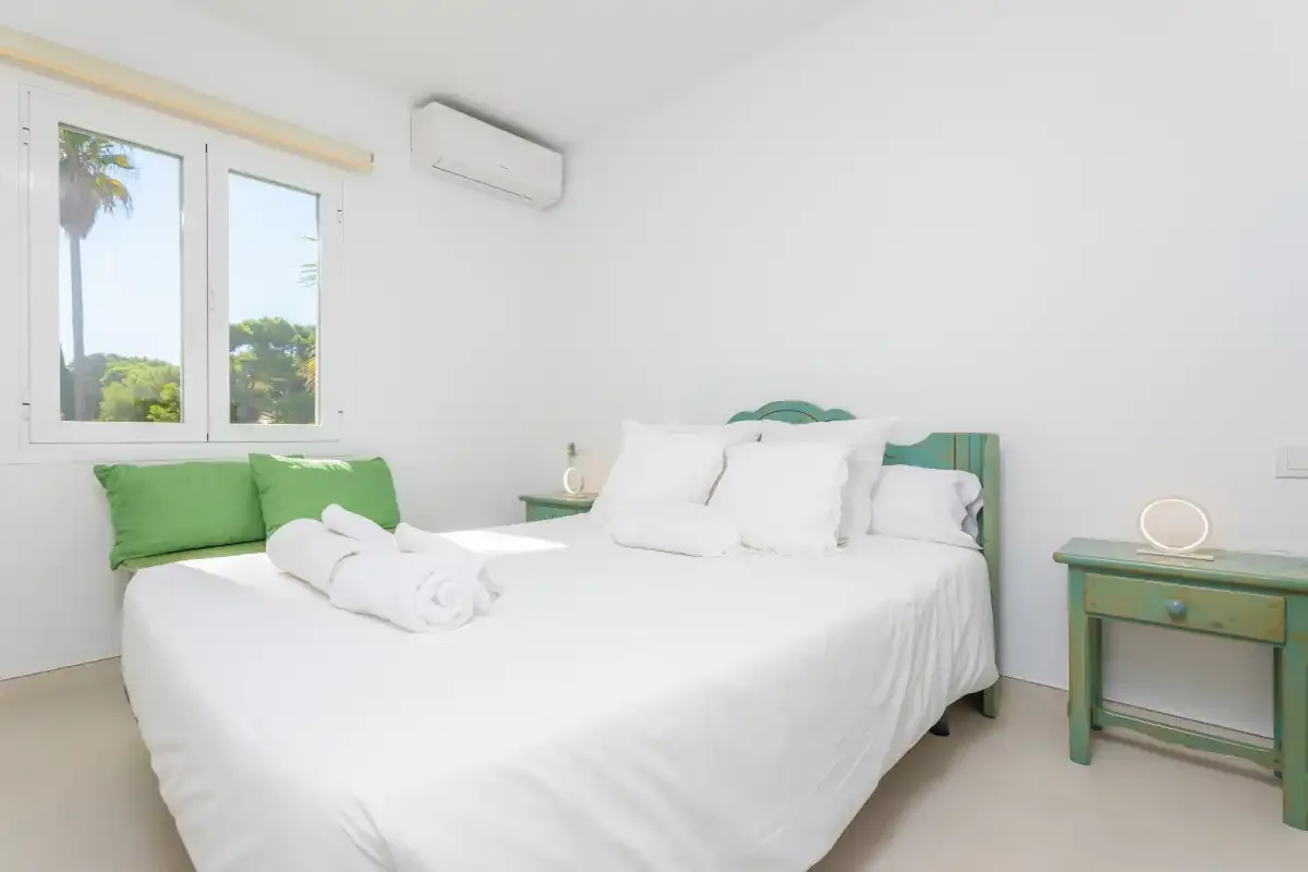 Un dormitorio con una cama blanca, un cabecero verde y una ventana.