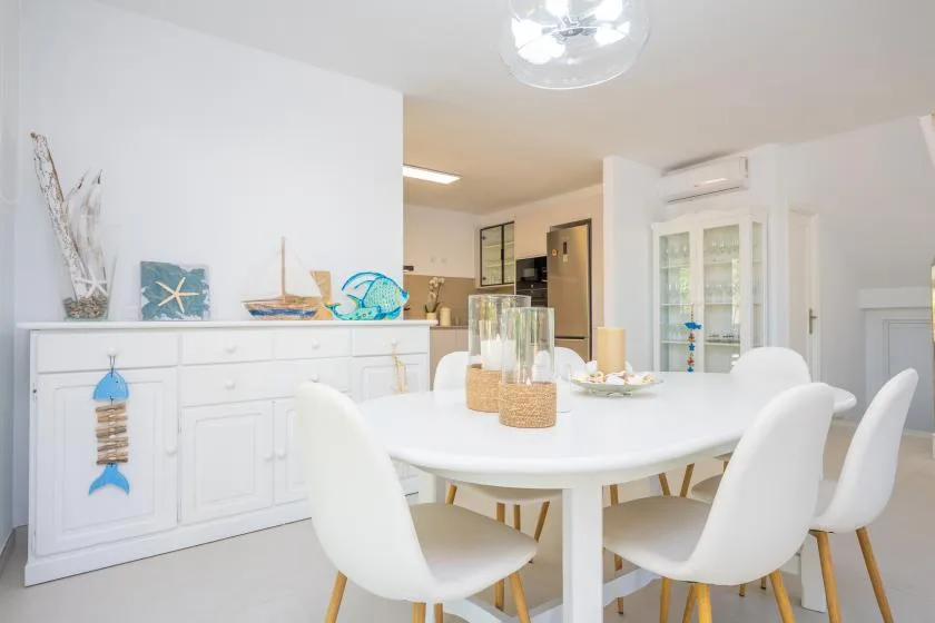 Un comedor luminoso con una mesa blanca y un aparador decorado con detalles costeros.