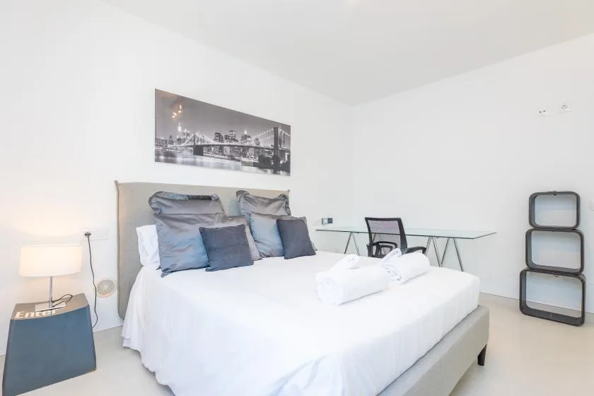 Un dormitorio luminoso con una cama bien arreglada y un escritorio de vidrio.