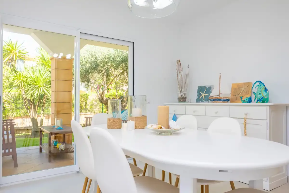 Un comedor luminoso con una mesa blanca junto a puertas de vidrio que dan a un patio.