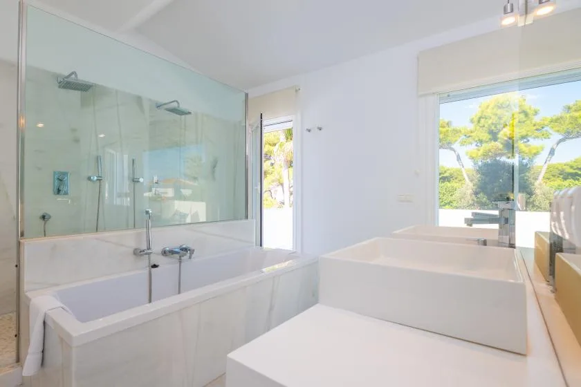 Un baño luminoso tiene una bañera junto a una amplia ducha de vidrio.