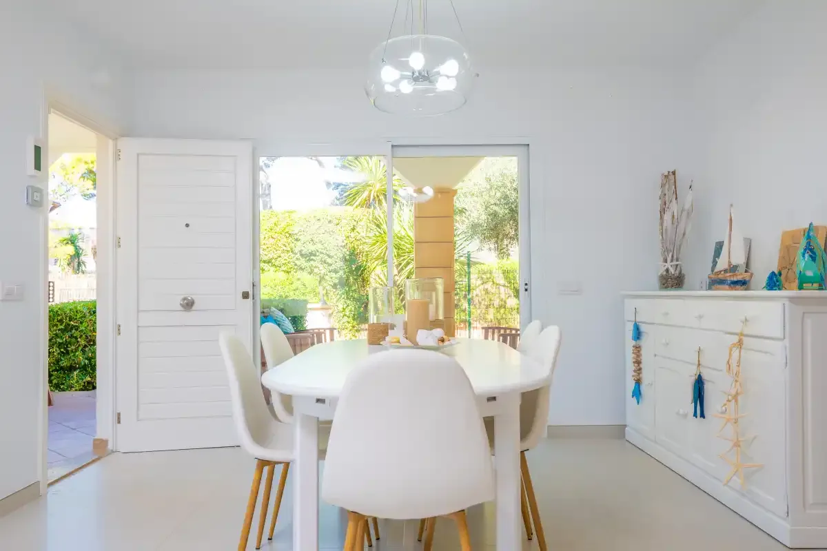 Un comedor luminoso con asientos blancos junto a puertas abiertas al jardín.