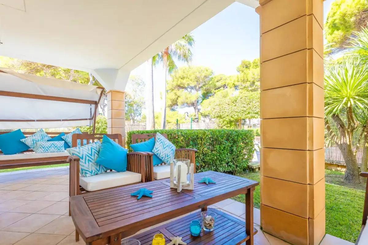 Un patio exterior cubierto tiene asientos acolchados y una mesa de madera.