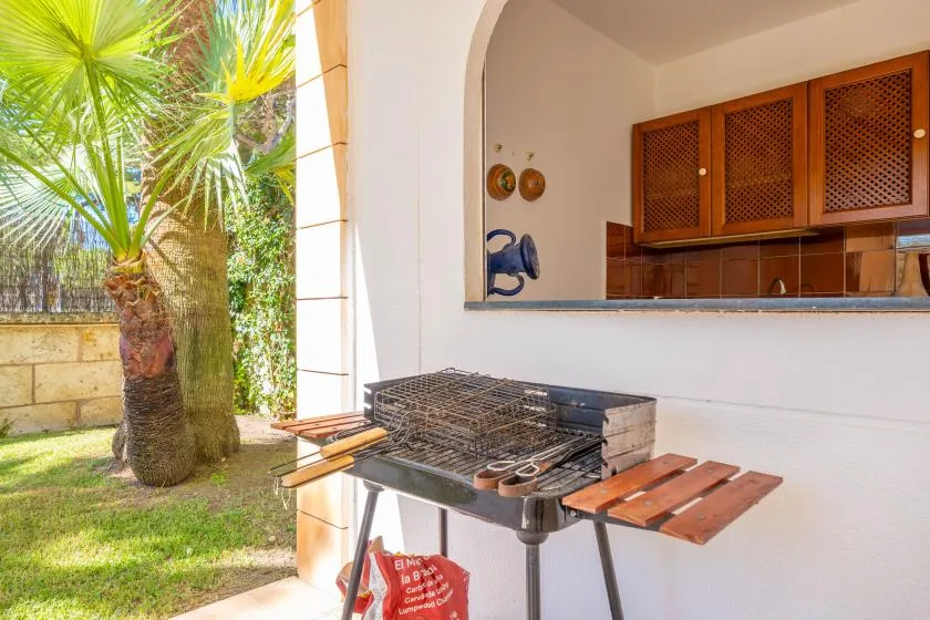 Una parrilla al aire libre está junto a un jardín soleado con palmeras.