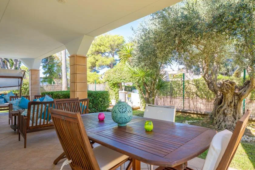 Zona de comedor exterior a la sombra, con una mesa de madera y vistas al jardín.