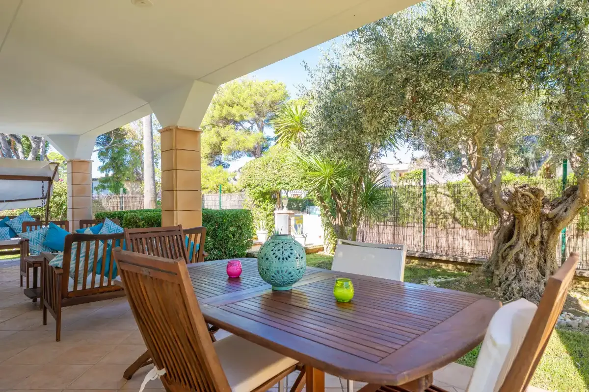 Comedor exterior cubierto con una mesa de madera y vistas al jardín.