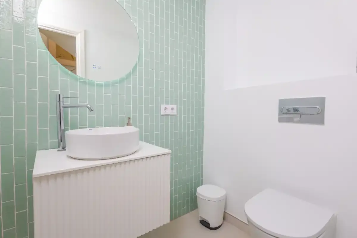Un baño con un espejo redondo sobre un lavabo de sobremesa y un inodoro.