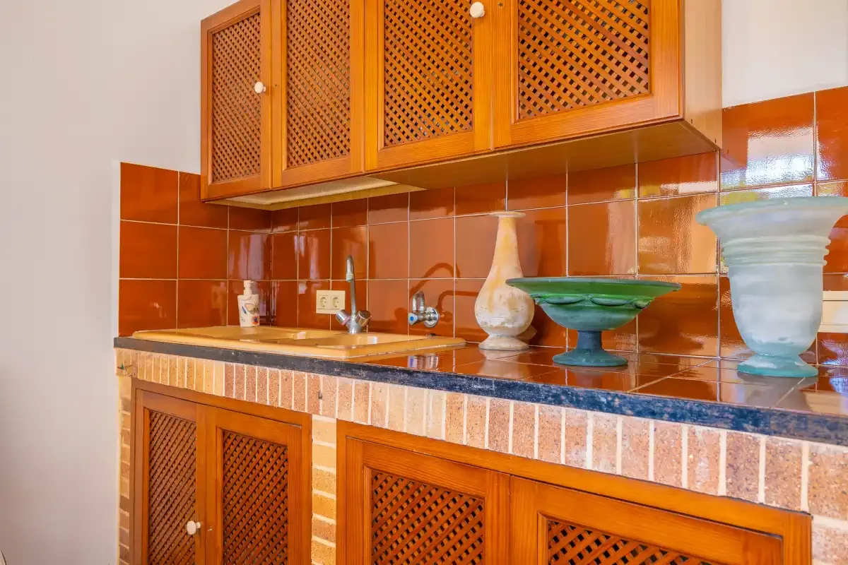 Una encimera de cocina alicatada está bajo armarios de madera con celosía.