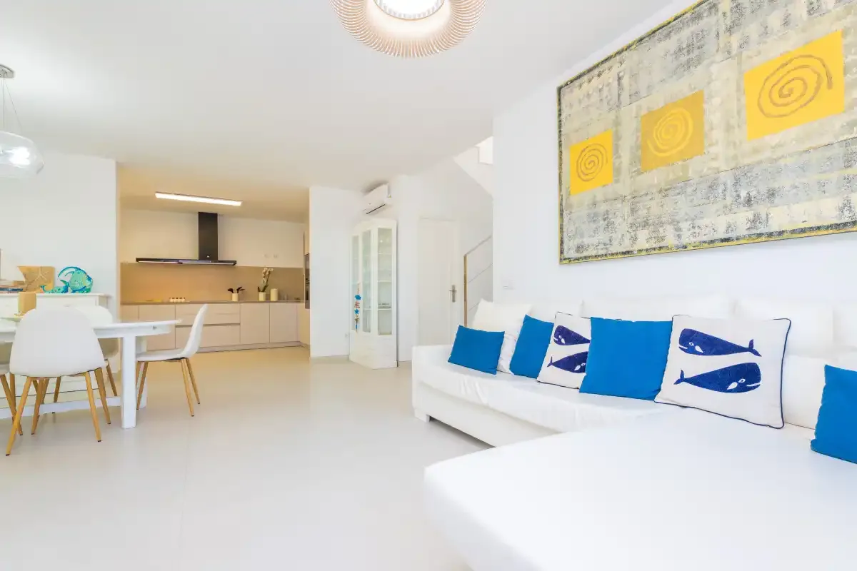 Un salón luminoso con asientos blancos y una cocina abierta.