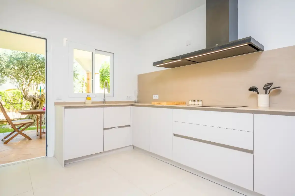 Una cocina luminosa y moderna con armarios blancos y una campana extractora ancha de acero inoxidable.