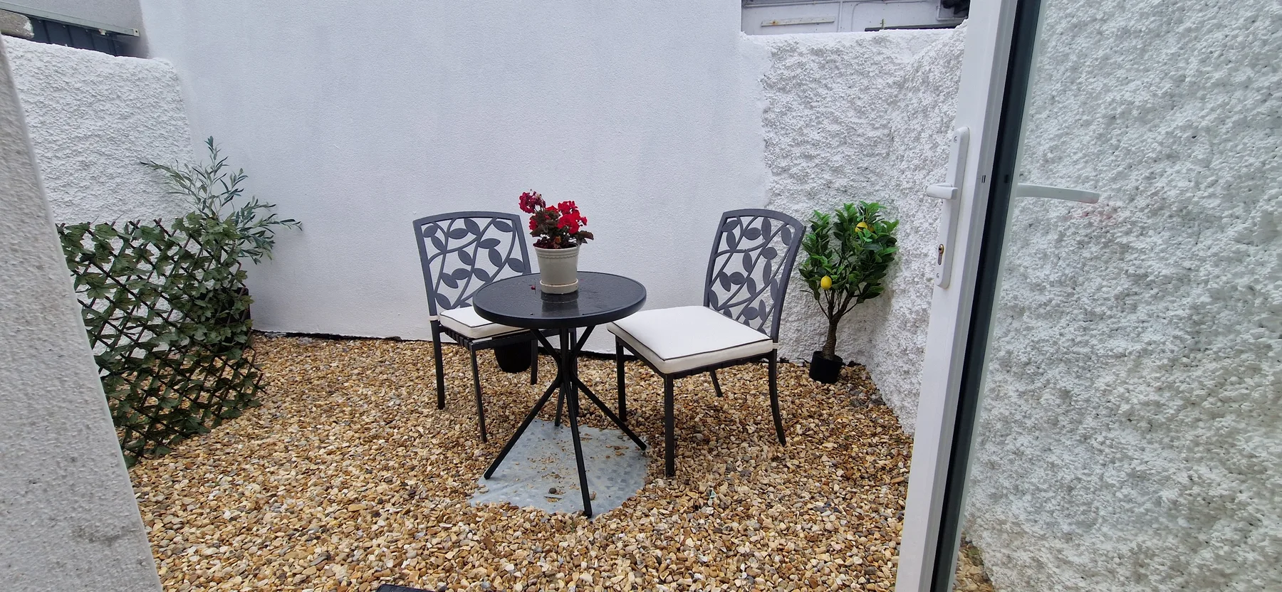 A small outdoor patio has a table and seating beside potted plants.