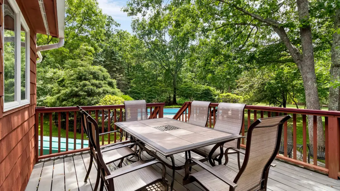 A wooden deck has a dining table and seating overlooking a wooded yard.