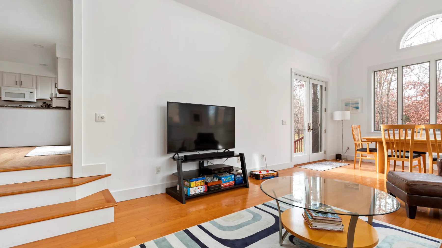 A bright living and dining area with a television, glass table, and large windows.