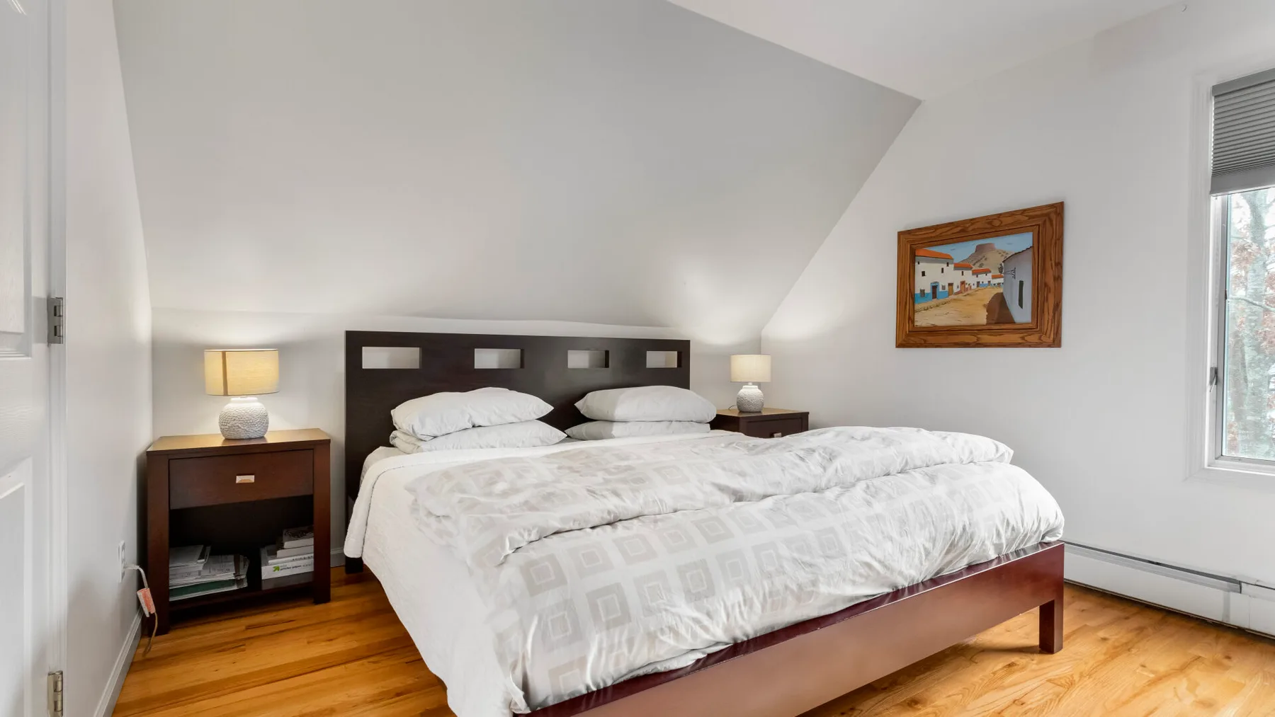 A bedroom with a double bed, bedside tables, and a sloped ceiling.