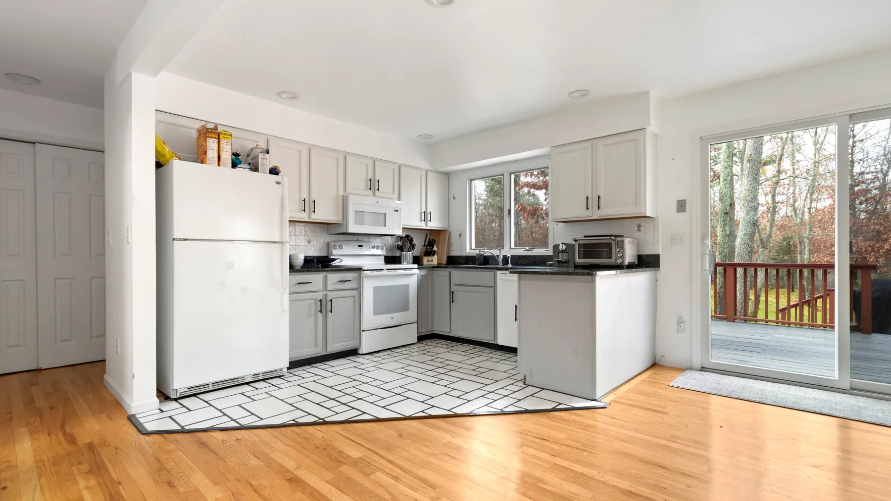 A bright kitchen with white cabinets and a sliding glass door opening to a deck.