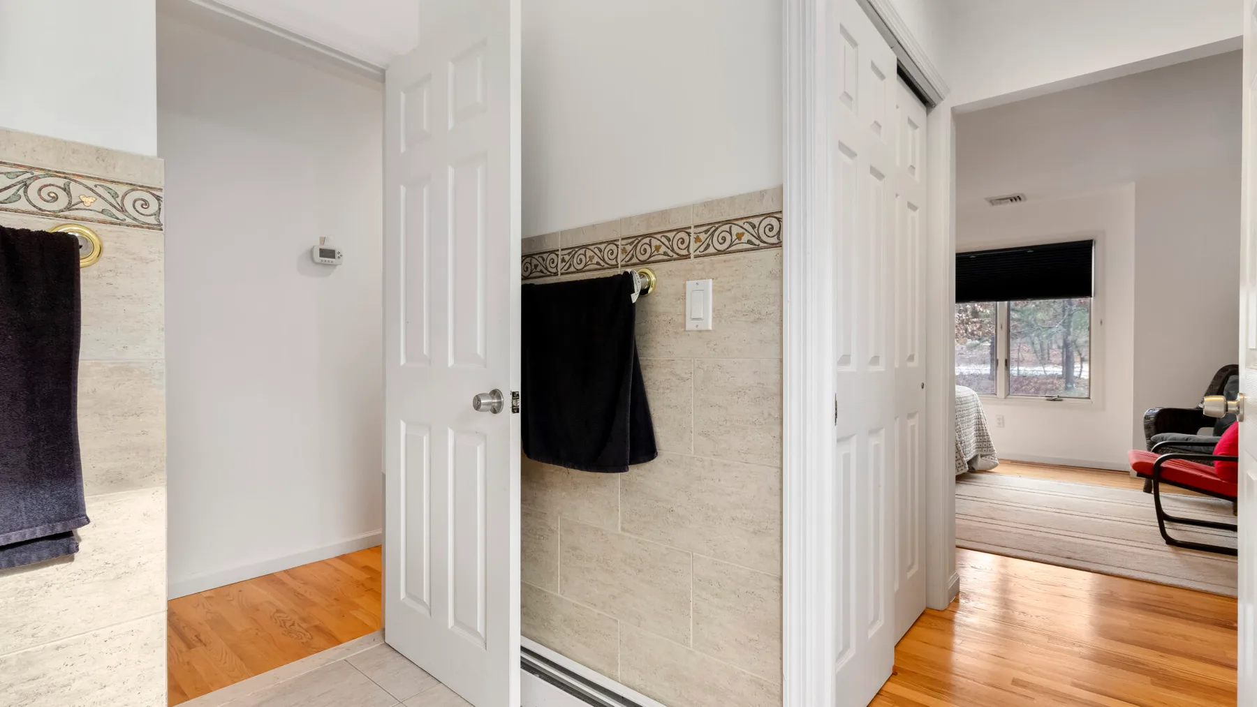 A bathroom with tiled walls and an open doorway leading to a bedroom.