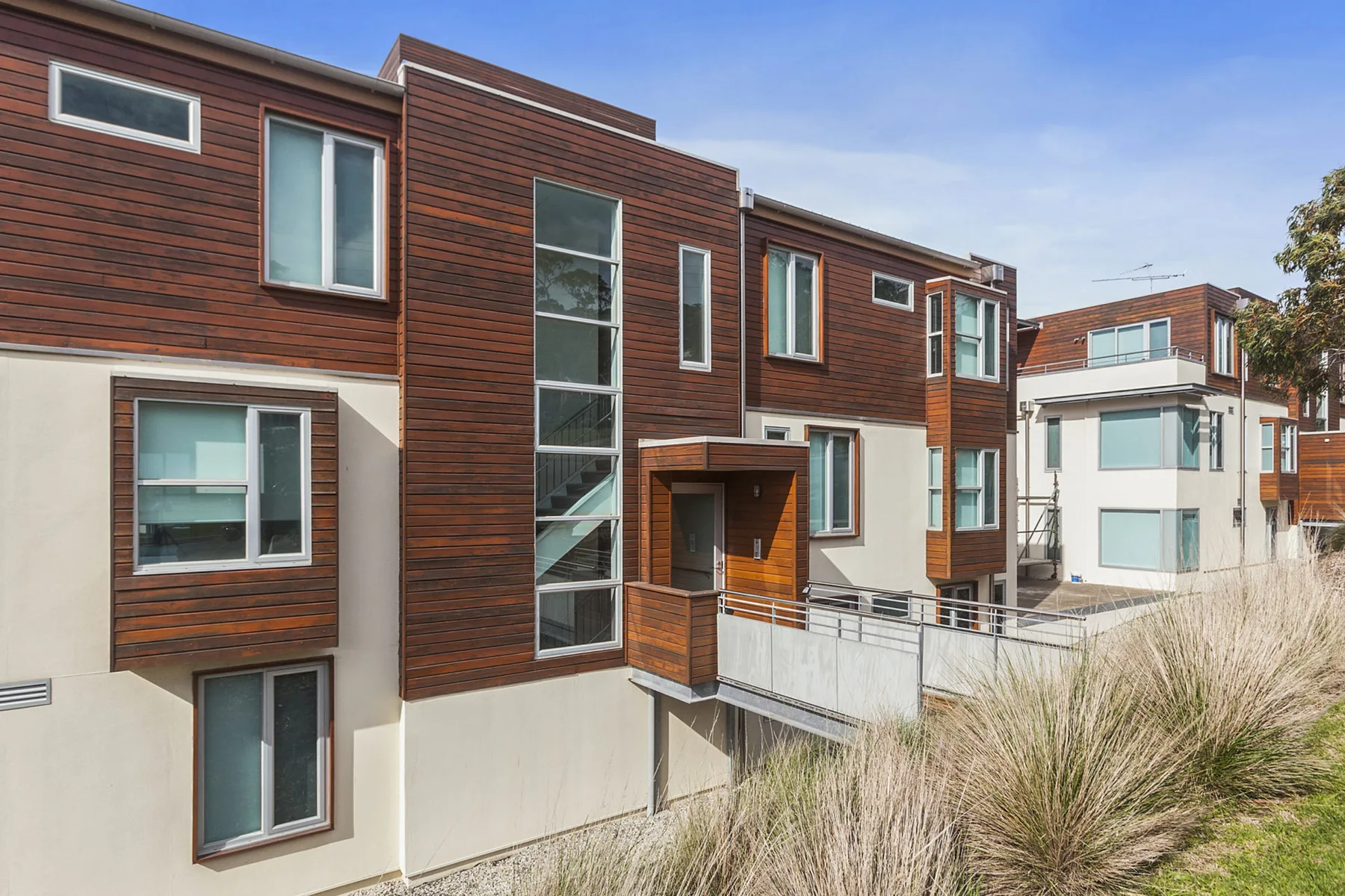 Modern apartment buildings with wood-toned siding and large windows under a clear sky.