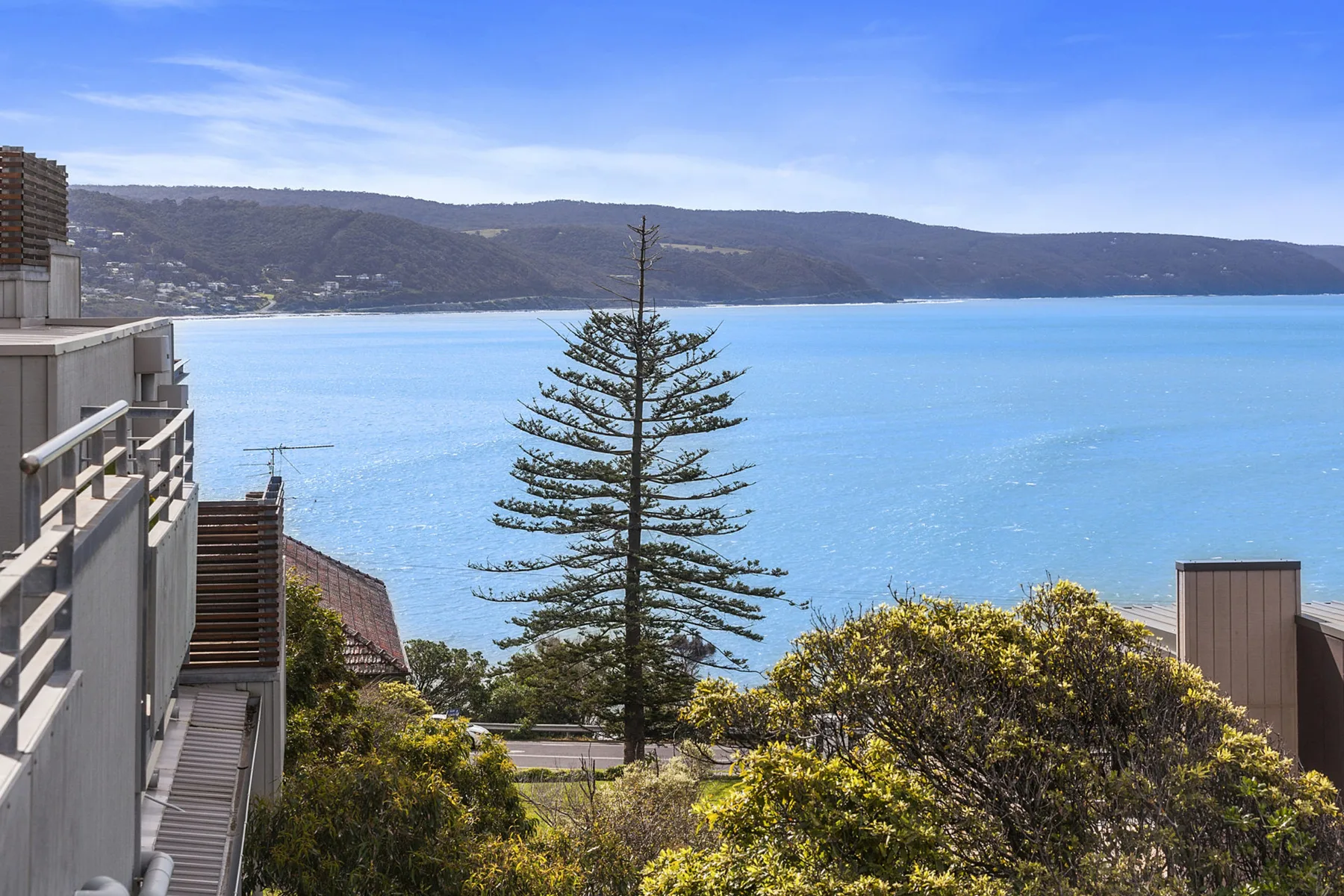 A coastal view shows blue water, a distant shoreline, and trees.