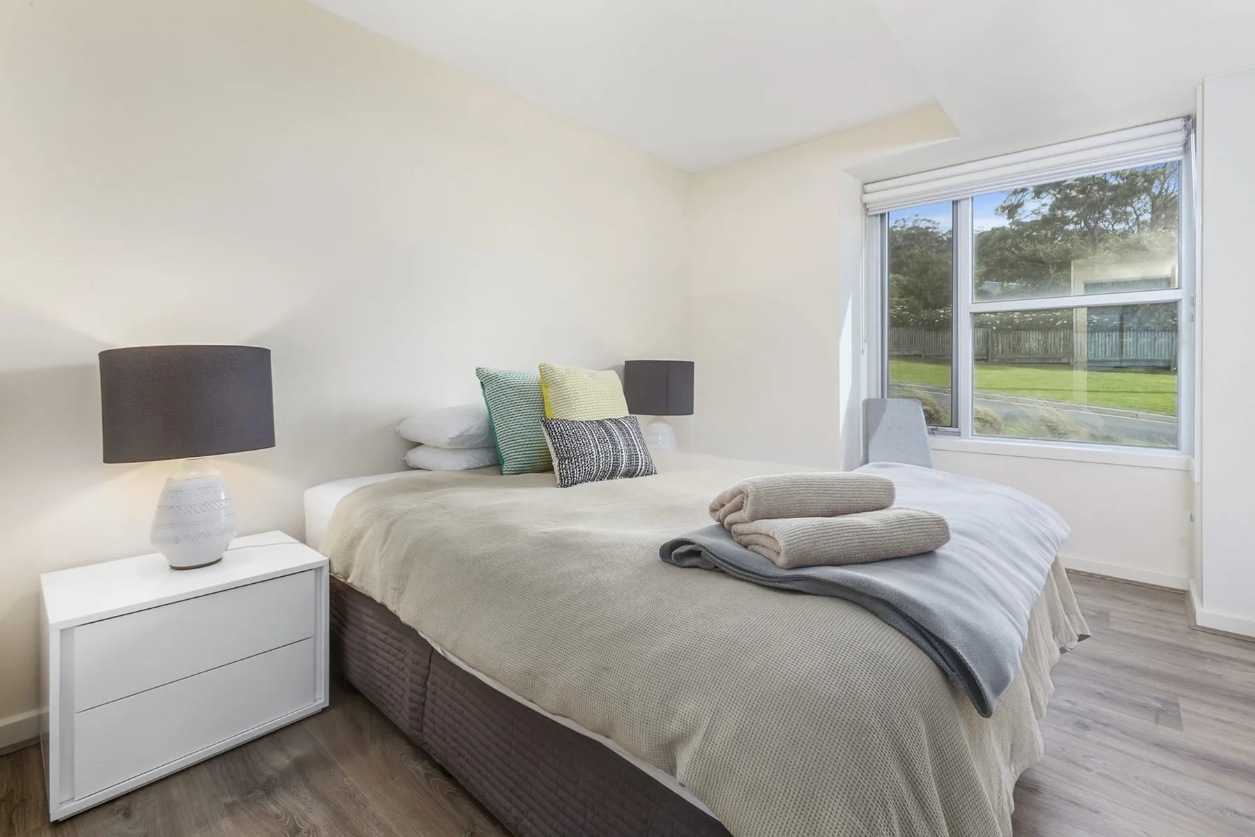 A bedroom with a neatly made bed beside a large window.