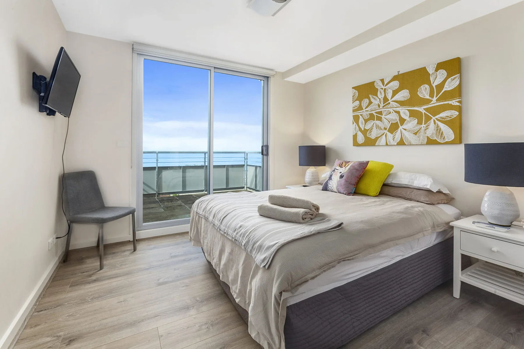 A bright bedroom with a large bed beside sliding glass doors opening onto a balcony.