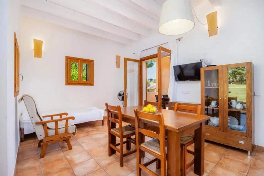 A bright dining and sitting area with a wooden table and chairs beside an open doorway.