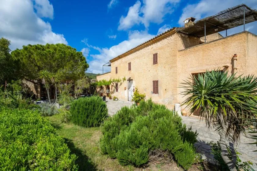 A stone building borders a landscaped garden with shrubs and trees.