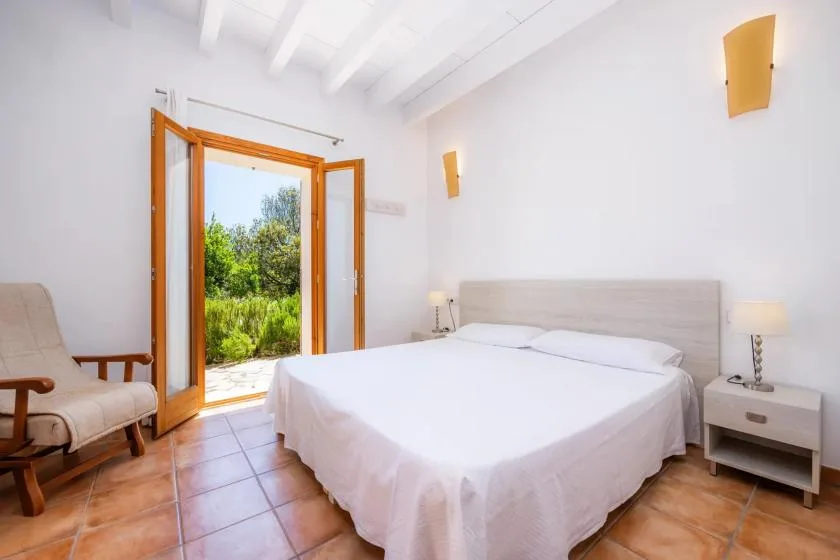 A bright bedroom with a neatly made bed and open doors to greenery.