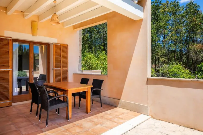 A covered outdoor dining area with a wooden table and seating beside open windows.