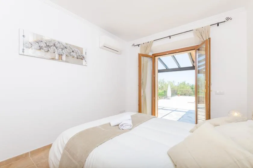 A bright bedroom with white bedding and open wooden-framed doors to a patio.