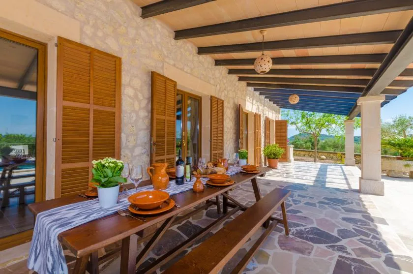 A covered outdoor dining area with a long table and wooden shutters.