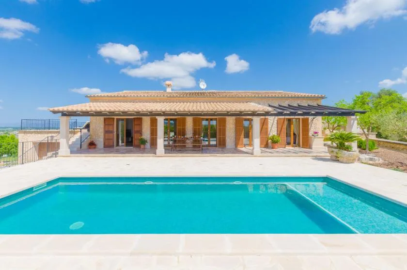 A swimming pool sits in front of a house with a covered patio.